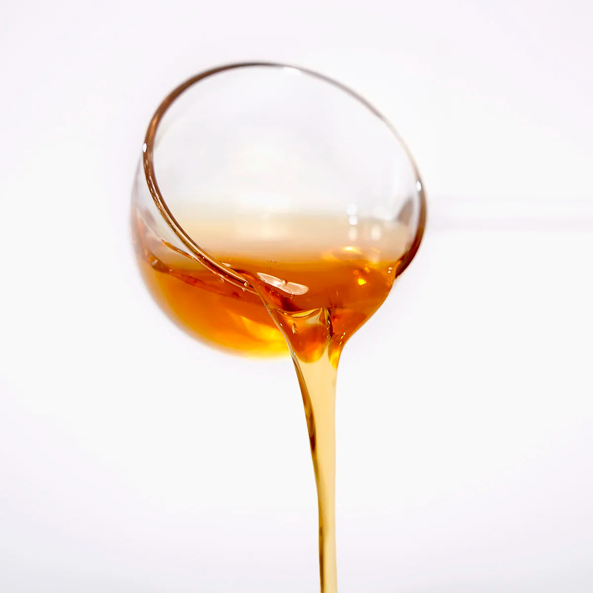 Golden Longan Honey Syrup pouring from a glass cup, showing its smooth texture and flow.
